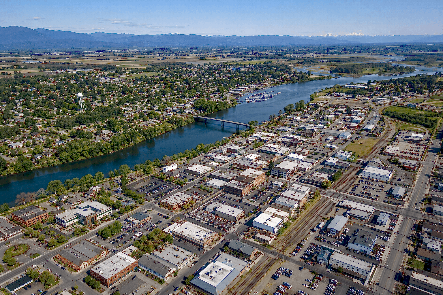 burlington-wa-aerial-view-skagit-county-washington Aerial view of Burlington, WA featuring downtown buildings, the Skagit River, surrounding neighborhoods, and mountain views in Skagit County, Washington